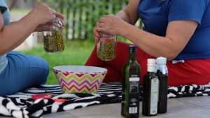 Two women mixing chamomile with oil outdoors for a natural remedy.